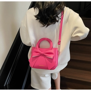 Detail of rose red bow tote bag with adjustable strap worn by a model in back view