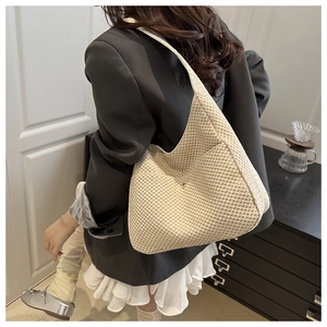 Dettaglio di una borsa tote intrecciata beige con focus su trama e tracolla larga