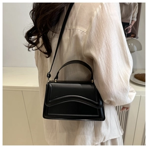 Détail du petit sac carré en cuir noir avec coutures ondulées sur le rabat avant