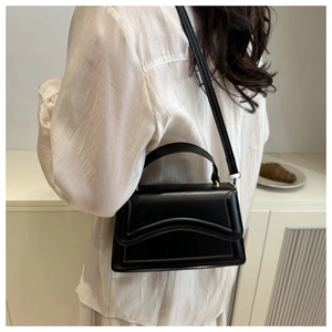 Dettaglio di un'elegante borsa a mano nera con patta ondulata dal design minimalista