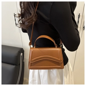 Détail d'un sac bandoulière marron en cuir avec plis en arc et finitions métalliques dorées