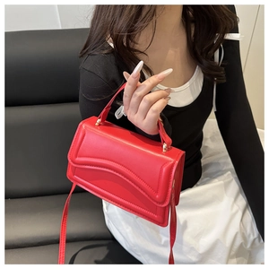 Détail du sac rouge avec coutures ondulées sur le rabat comprenant poignée et bandoulière