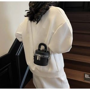 Détail d'un mini sac cylindrique noir avec fermetures éclair argentées et chaîne