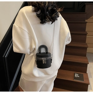 Detail of black leather bucket bag with contrast white stitching and silver chain strap