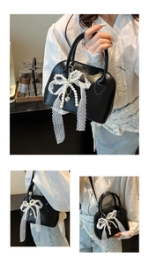 Detail of black shell-shaped Boston bag with pearl lace bow and silver heart pendant