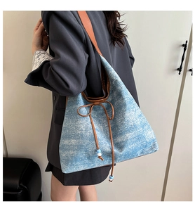 Close-up of large denim tote bag featuring brown leather drawstring and beaded details