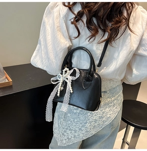Detailansicht der schwarzen Handtasche mit Perlen- und Spitzenanhänger am Schultergurt