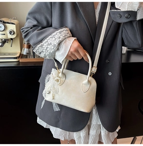 Detailansicht der cremefarbenen Ledertasche mit Spitzenbesatz, Perlenkette und Herz
