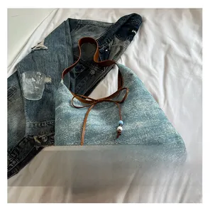 Detail of blue denim tote bag with brown leather trim and beaded bow decoration