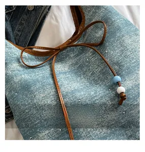 Close-up of denim tote bag featuring rhinestone detailing and brown leather drawstring