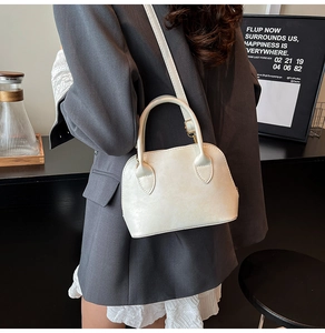 Nahaufnahme einer cremefarbenen Bowlingtasche getragen von einem Modell mit grauem Blazer
