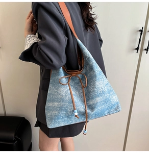 Detail of blue denim tote bag with brown faux leather strap and bow drawstring