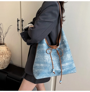 Detail of light blue tote bag with brown leather trim and beaded bow decoration