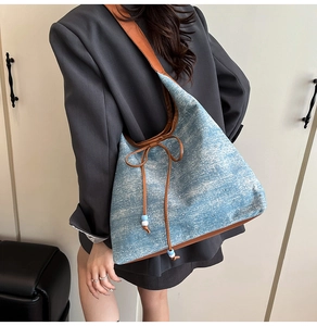 Detailed view of blue denim tote bag with brown leather trim and rivet accents