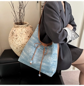 Detail of vintage denim tote bag featuring brown leather trim and beaded bow drawstring