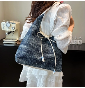 Detail of blue denim shoulder bag with white beads and drawstring bow on side
