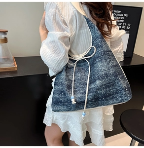 Detail of denim shoulder bag with white bow drawstring and light blue bead accents