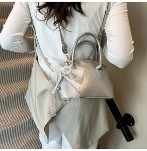 Detailansicht einer silbernen Muscheltasche mit Perlen und Spitzen-Schleifen-Anhänger