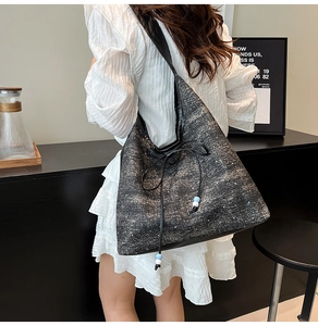Detail of dark tweed tote bag with bow drawstring and blue bead accents on white dress