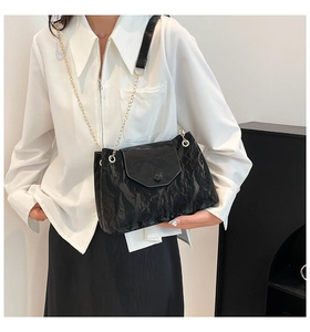 Details einer schwarzen glänzenden Schultertasche mit goldener Kette am Model