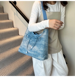 Detail of light blue denim tote bag with bow tie and beaded tassels worn by a model