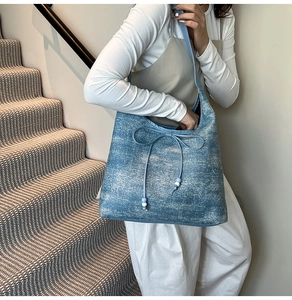 Close-up of blue denim hobo bag with bow ribbon and beaded details worn by a model
