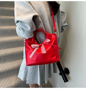 Dettaglio borsa a secchiello rossa in pelle con fiocco in pizzo bianco e tracolla regolabile