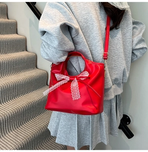 Dettaglio borsa a secchiello in pelle rossa con fiocco in pizzo bianco e tracolla rimovibile