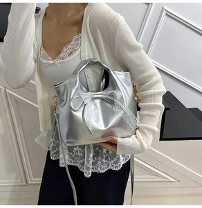 Dettaglio di una borsa a secchiello argento con grande fiocco di pizzo e finitura metallica