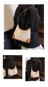 Détail du sac sous l'aisselle en toile crème avec garniture en cuir marron et breloque cerf