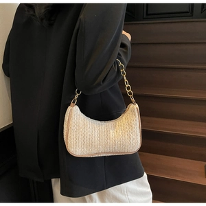 Detail of woven beige underarm bag with brown leather trim and golden chain strap