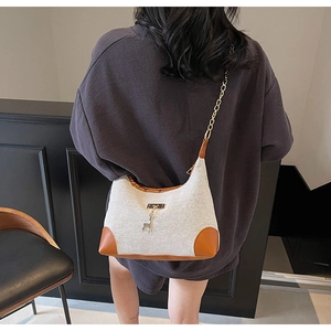 Détail d'un sac bandoulière en toile avec bordure en cuir brun et pendentif cerf doré