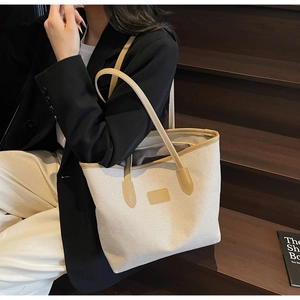 Detail of the large canvas tote bag with leather trim worn over the shoulder by a model