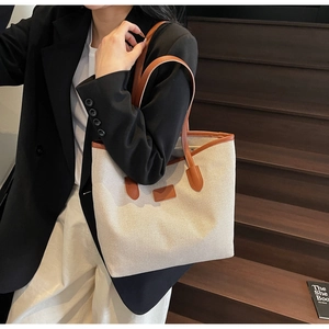 Detail of canvas tote bag with brown leather trim carried by a model in a blazer