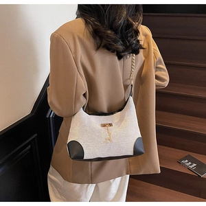 Détail du sac sous le bras en toile avec bordure en cuir noir et pendentif cerf doré