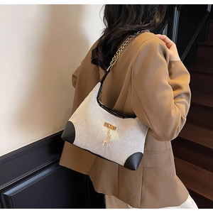 Detail of grey canvas crossbody bag with chain strap worn with a camel blazer
