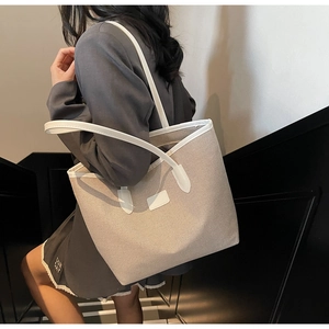 Close-up of a large beige straw tote bag with white leather trim and sturdy dual shoulder straps