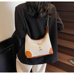 Détail du sac bandoulière en toile avec garniture en cuir brun et pendentif cerf doré