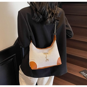 Détail du sac cabas en toile avec bordure en cuir marron et breloque cerf doré sur modèle