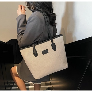 Detail showing the textured beige canvas and black leather trim of the large tote bag