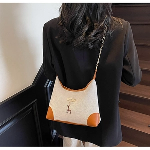 Détail du sac en toile avec bordure en cuir marron, chaîne en métal et breloque cerf