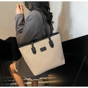 Close-up of beige woven tote bag with black leather straps and textured canvas detail