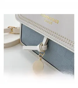 Detail of blue textured leather bag with white flap and golden metal pendant