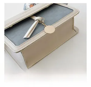 Close-up of beige leather shoulder bag with fine stitching and golden metal pendant