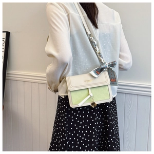 Detail of crossbody bag featuring cream and green contrast leather with silk scarf accent