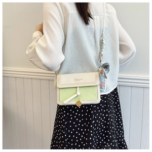 Detail of cream crossbody bag with floral scarf strap and gold pendant on the side