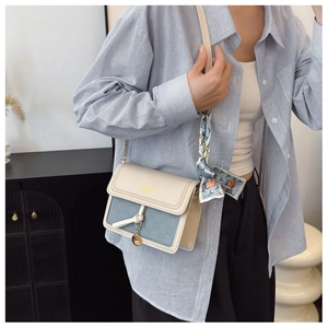 Detail of a square leather bag with a stylish silk scarf handle and golden ornament