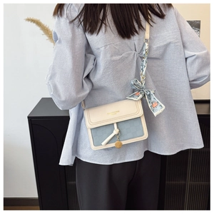 Detail view of cream and blue crossbody bag with silk scarf and gold pendant detail