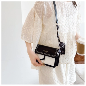 Detail of a black and white square crossbody bag with silk scarf and gold pendant