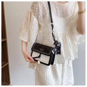 Detail of bicolour crossbody bag featuring logo print and decorative silk scarf accessory